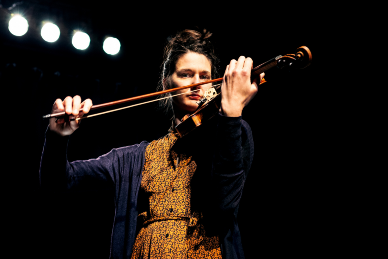 Dorothée Royez steht auf der dunklen Bühne im Scheinwerferlicht und spielt Geige.