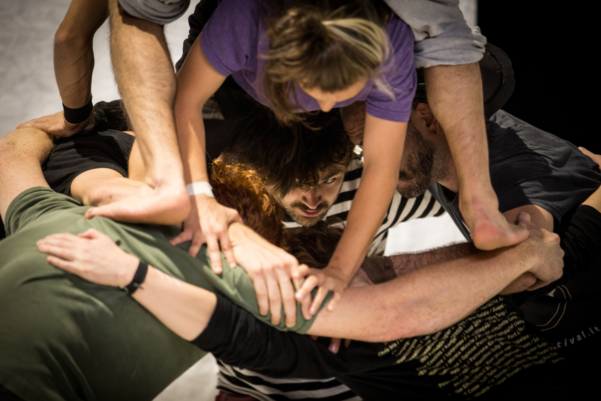 Eine Nahaufnahme aus dem Probenraum: Die Artist*innen bilden eine Körperskulptur. Sie klettern aufeinander, greifen sich an Händen und Schultern, bis nicht mehr zu erkennen ist, welche Arme zu welchem Körper gehören. 